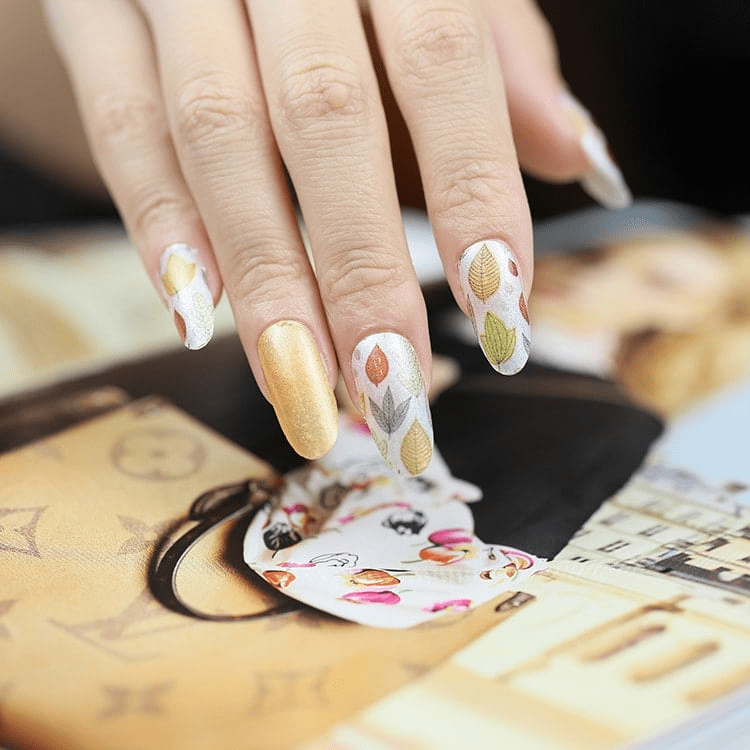 Hand wearing autumn leaf nail wraps showing yellow orange botanical nail art design