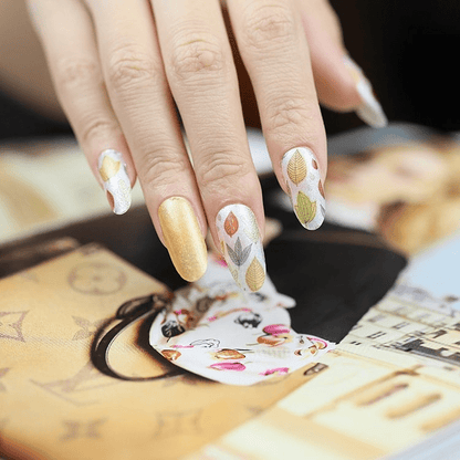 Hand wearing autumn leaf nail wraps showing yellow orange botanical nail art design