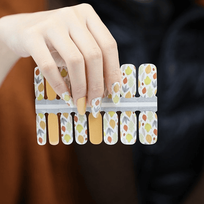 Hand holding autumn leaf pattern nail wraps with orange and yellow botanical designs