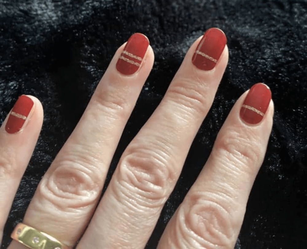 Close-up red nail wraps with gold accent stripes on fingers showing classic manicure design