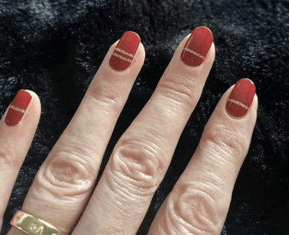 Close-up red nail wraps with gold accent stripes on fingers showing classic manicure design