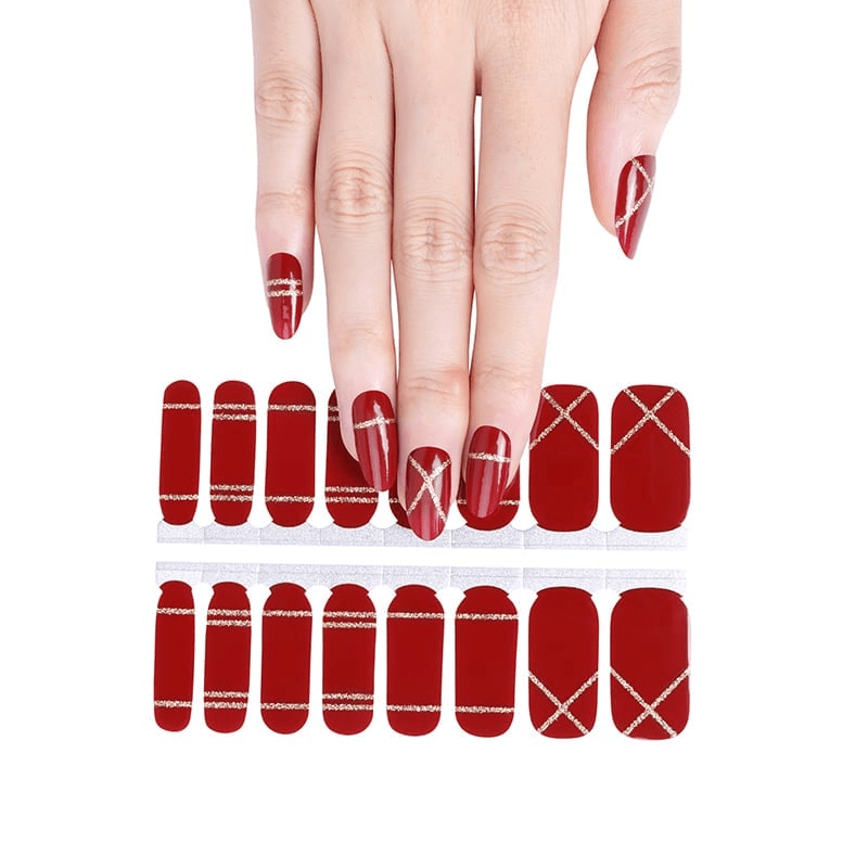 Hand displaying red nail wraps with gold metallic stripe patterns for at-home manicure