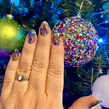 Hand wearing holographic rainbow glitter nail wraps with multicoloured sparkles and Christmas baubles