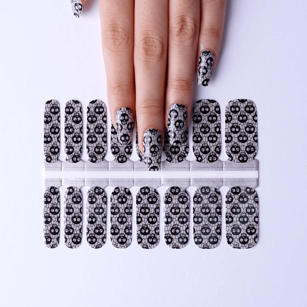 Sheet of gothic skull fishnet nail wraps with hand showing applied design