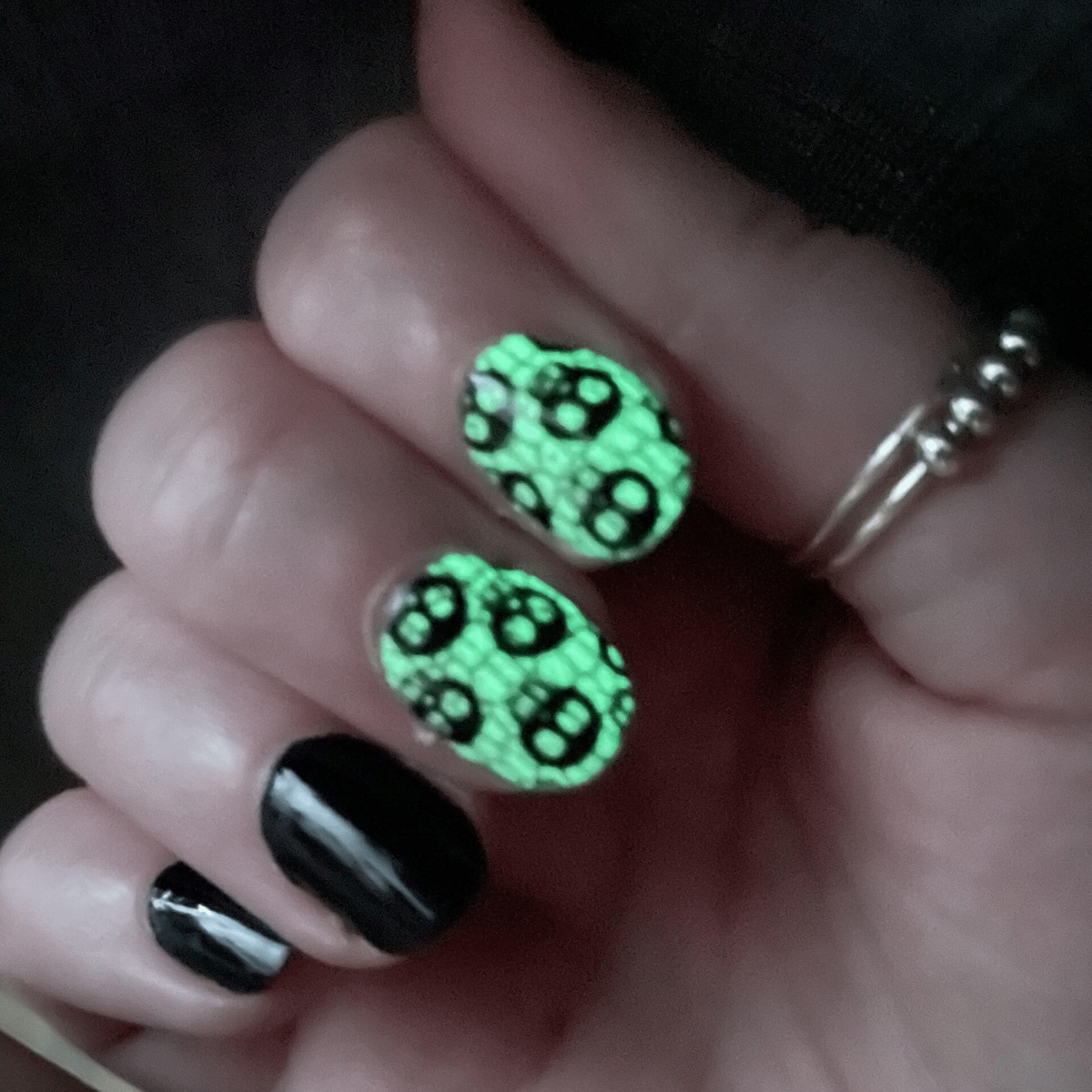 Green glow in the dark skull pattern nail wraps on hand with black accent nails