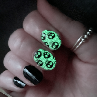 Green glow in the dark skull pattern nail wraps on hand with black accent nails