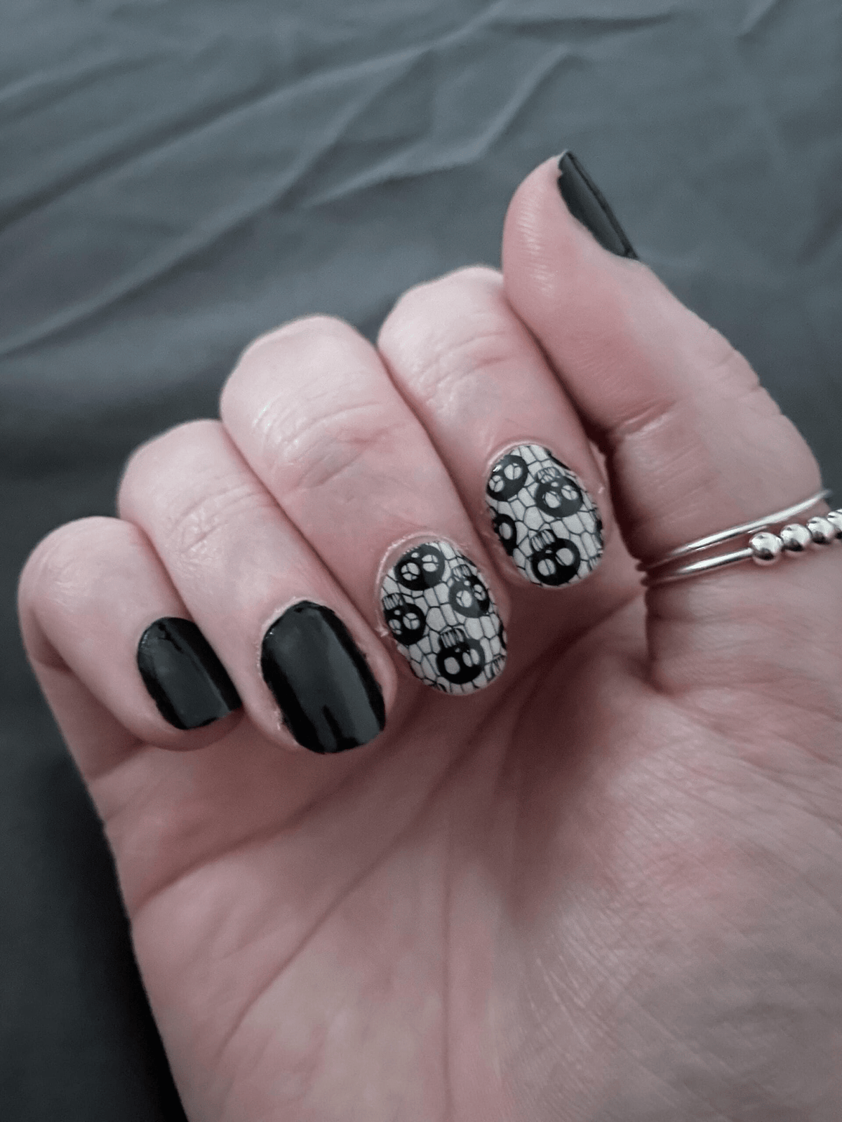 Gothic skull fishnet nail wraps on hand with black nails for Halloween manicure