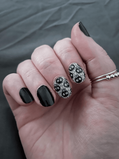 Gothic skull fishnet nail wraps on hand with black nails for Halloween manicure