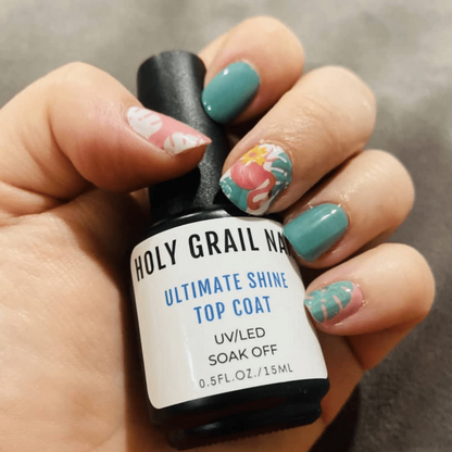 Hand holding UV top coat bottle displaying tropical flamingo and floral nail wraps in coral and teal