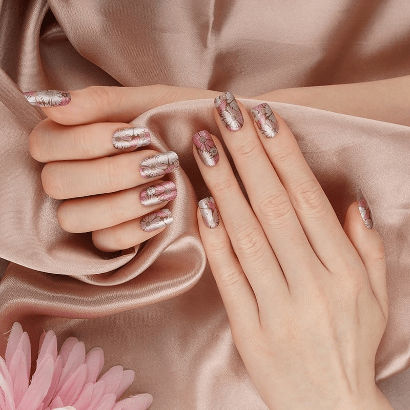 Hands with rose gold metallic nail wraps displaying shimmery pressed flower design against silk fabric