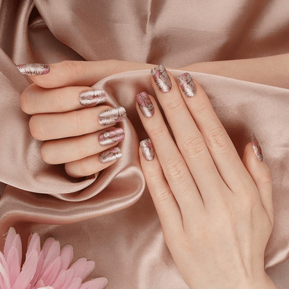 Hands with rose gold metallic nail wraps displaying shimmery pressed flower design against silk fabric