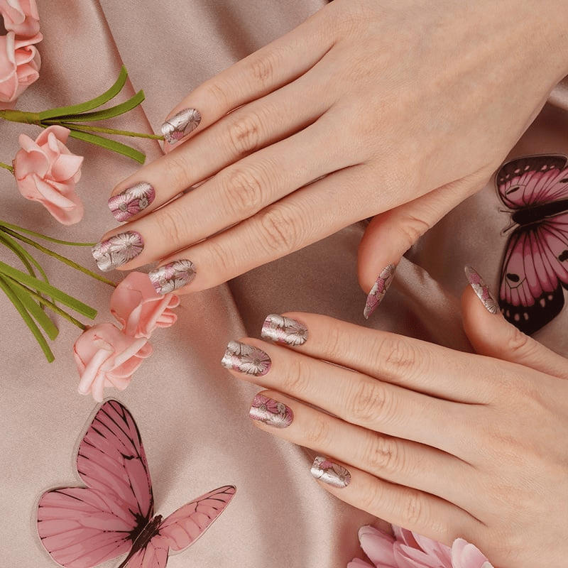 Pink floral nail wraps with pressed flower pattern on hands with butterfly decorations