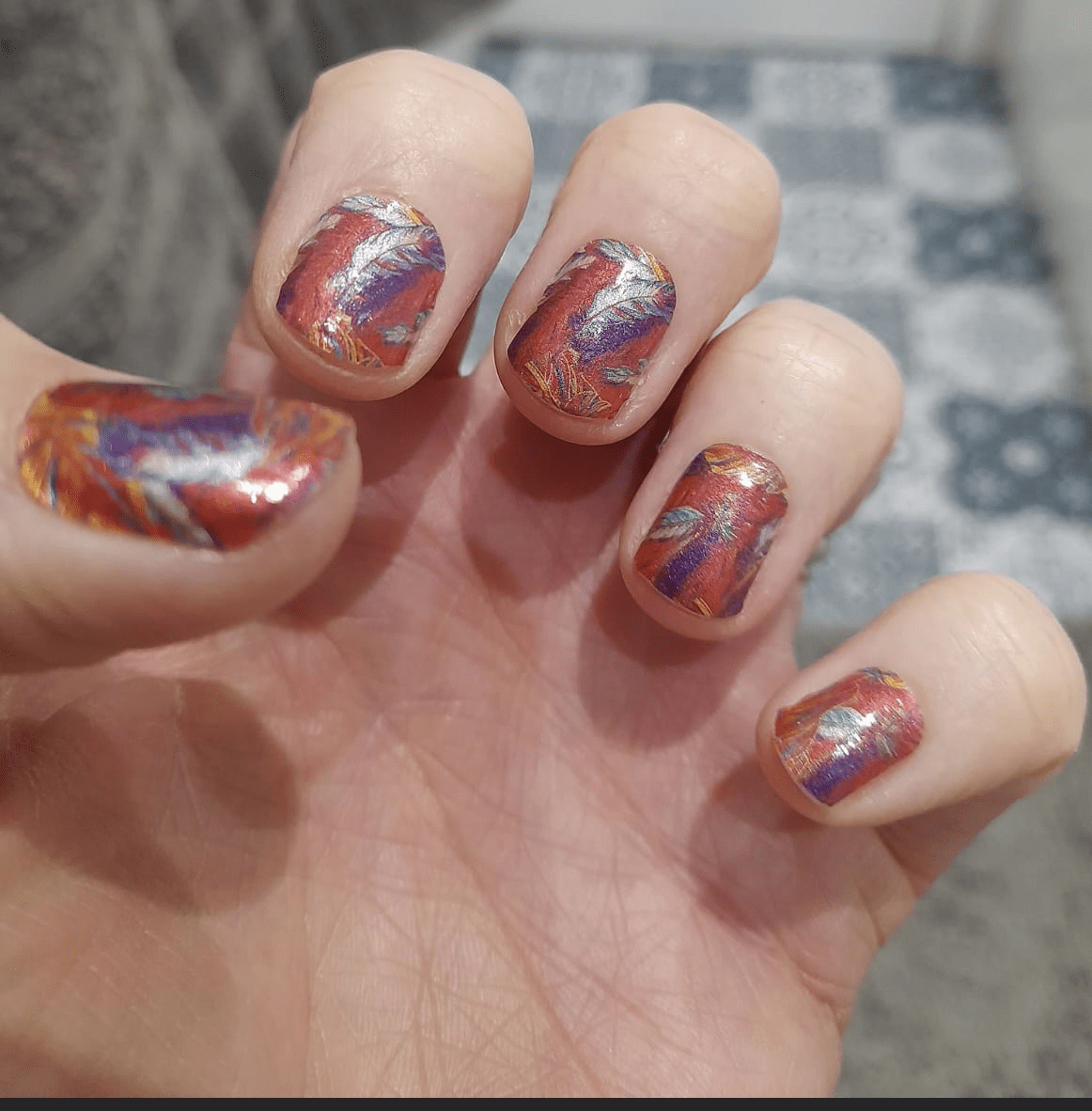 Vibrant feather pattern nail wraps on hand showing red orange blue gradient manicure design