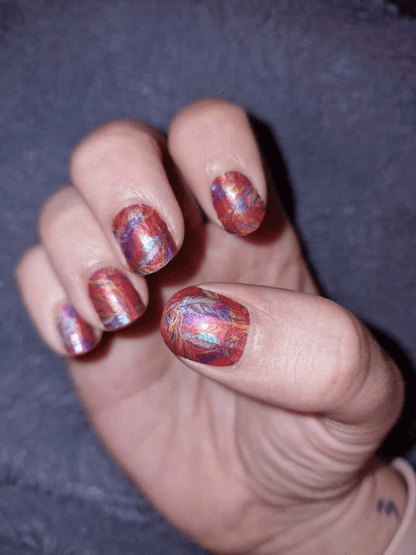 Multicoloured feather nail art wraps with red blue orange gradient pattern on hand