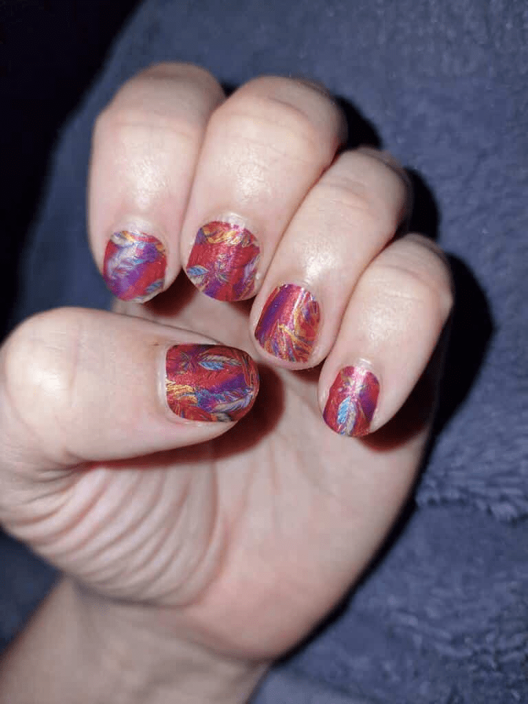 Artistic feather design nail wraps displaying vibrant red purple orange gradient colours on hand