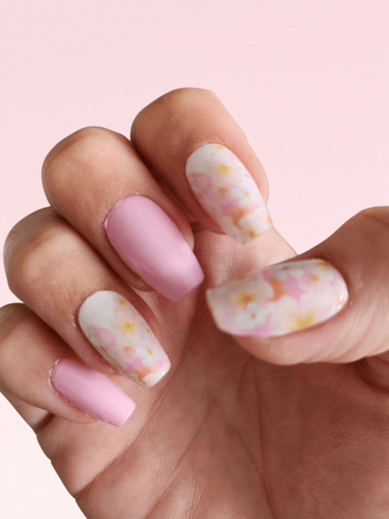 Pastel pink nail wraps with delicate floral pattern shown on hand