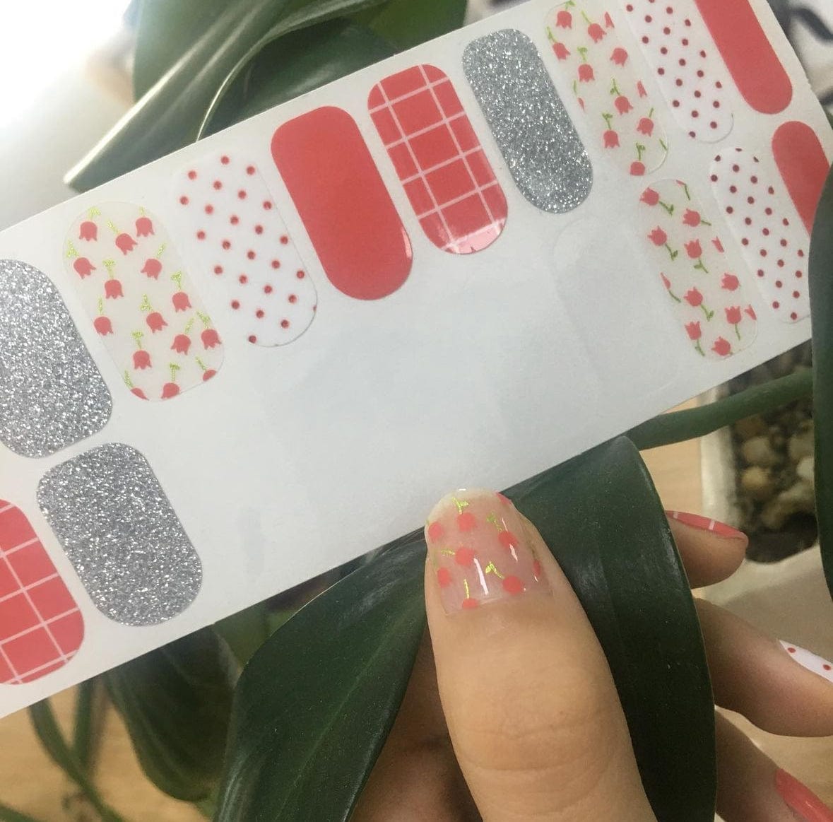 Mixed pattern nail wraps featuring red grid, silver glitter and floral designs held in hand