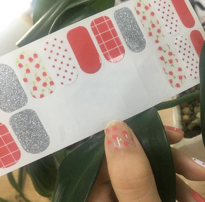 Mixed pattern nail wraps featuring red grid, silver glitter and floral designs held in hand