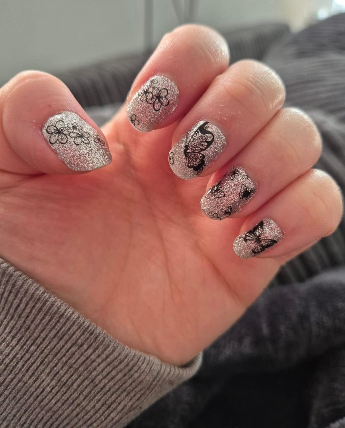Silver glitter nail wraps with black butterfly and floral line-art accents