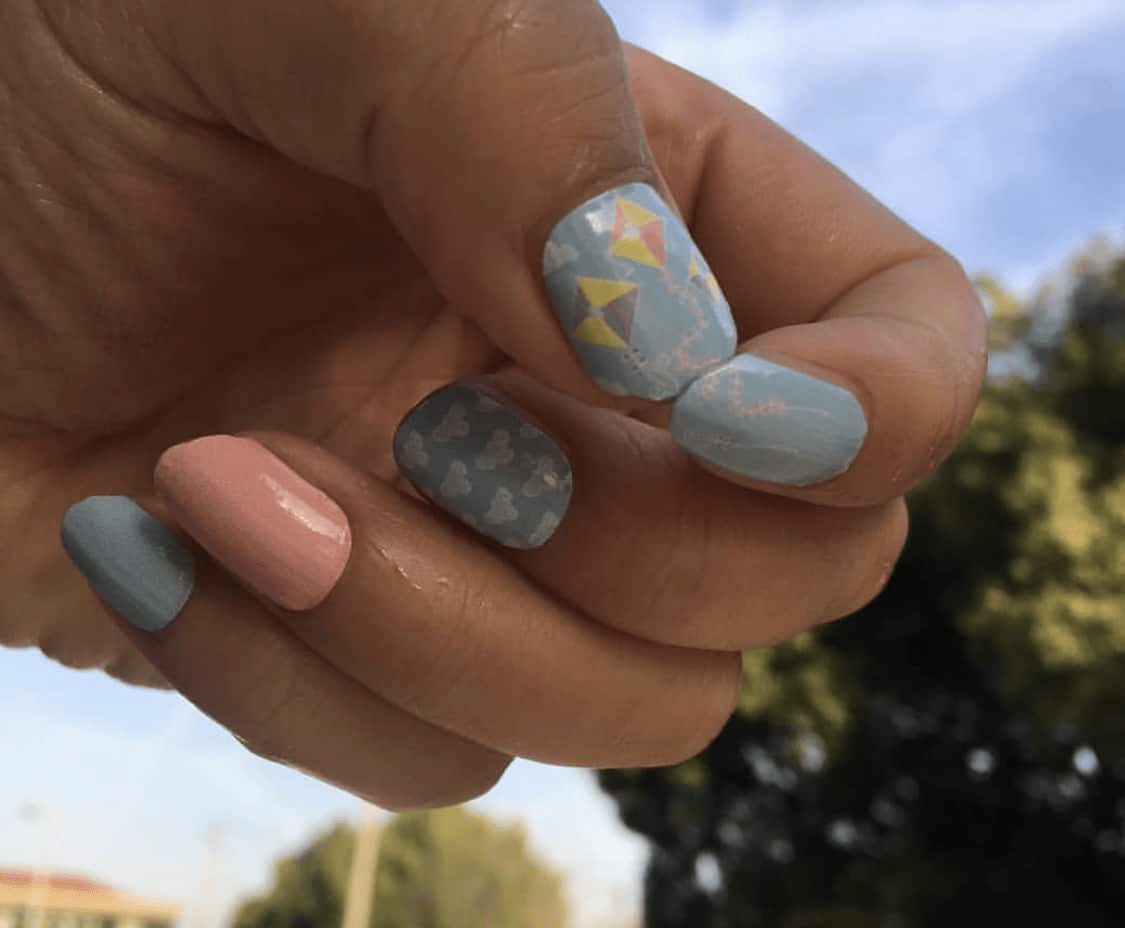 Hand wearing pastel blue kite nail art wraps with coral accent nail for spring manicure