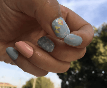 Hand wearing pastel blue kite nail art wraps with coral accent nail for spring manicure