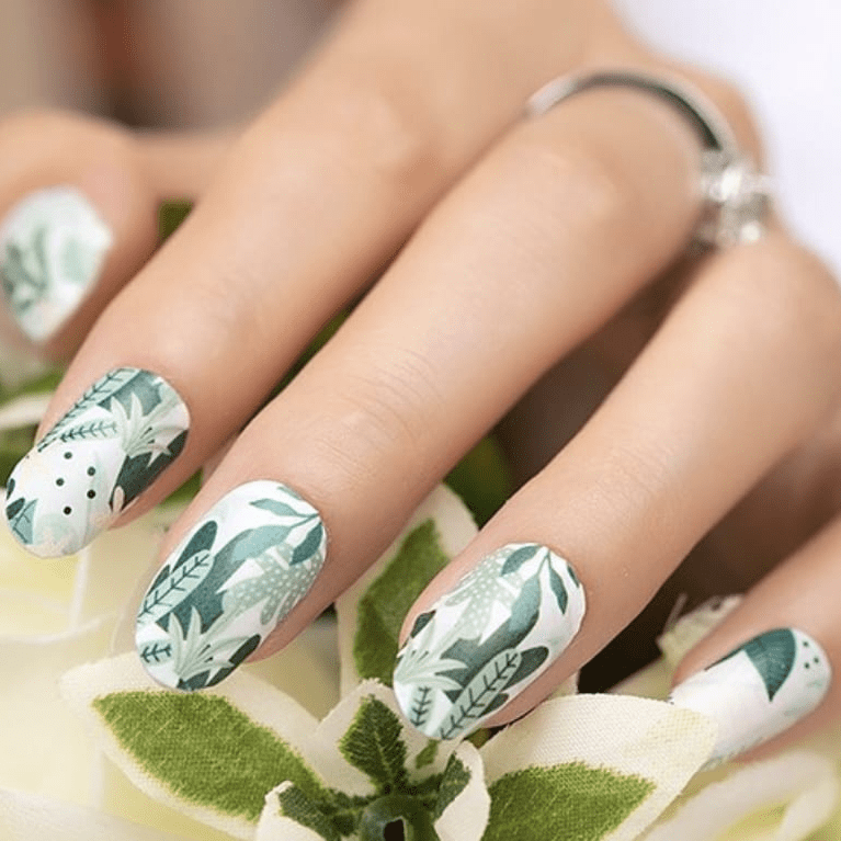 Hand wearing green botanical nail wraps with white background and leaf patterns