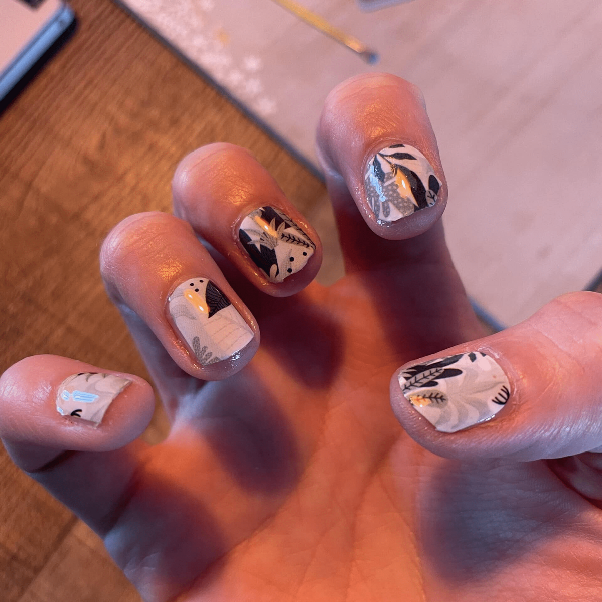 Hand displaying green and white botanical nail art with leaf pattern wraps