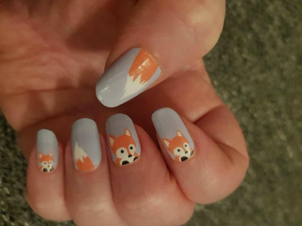 Close-up of fox nail wraps featuring orange cartoon fox faces on grey nail art
