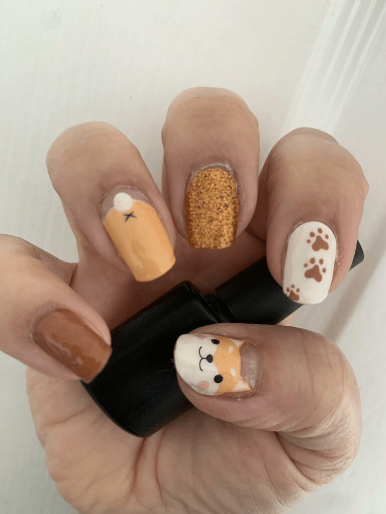 Hand wearing fox nail art wraps with orange glitter and brown paw designs