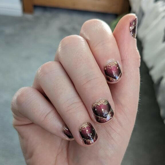 Burgundy and black nail wraps with gold glitter accents and marbled shimmer finish