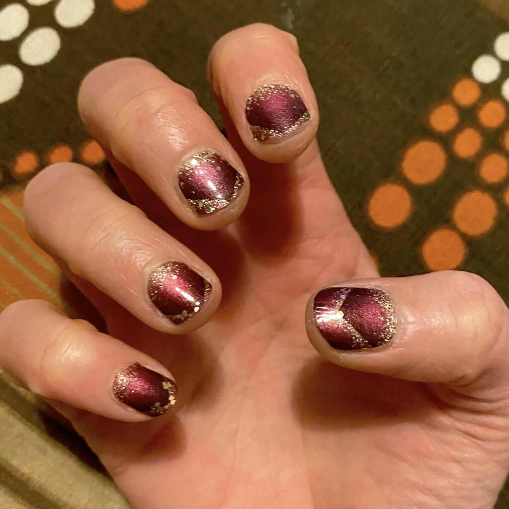 Burgundy chevron nail wraps with gold glitter on hand showing festive geometric manicure