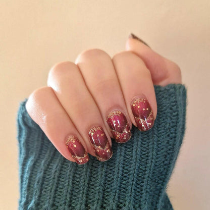 Hand in teal jumper showcasing burgundy and gold glitter nail wraps with geometric chevron nail art design