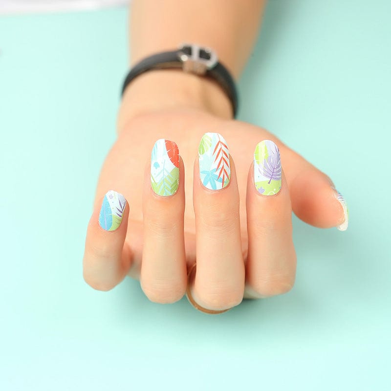 Hand wearing colourful botanical nail wraps with tropical leaf patterns in green and blue