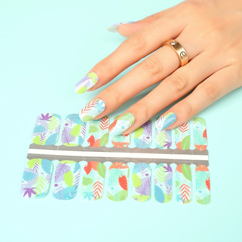 Hand applying botanical nail wraps with tropical leaf pattern in multicoloured design sheet