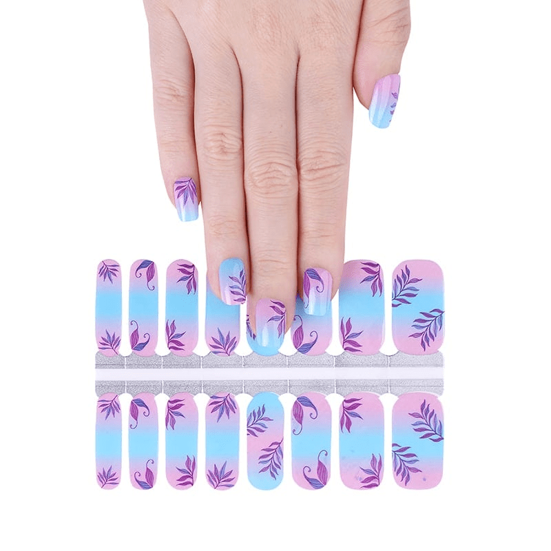 Hand applying botanical nail wraps from sheet showing purple leaves on blue pink gradient