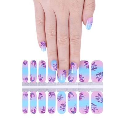 Hand applying botanical nail wraps from sheet showing purple leaves on blue pink gradient