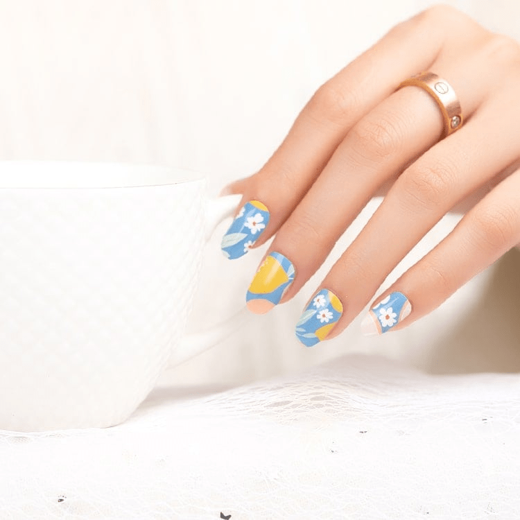 Hand wearing cheerful blue nail wraps with white flowers and fruit pattern for colourful manicure