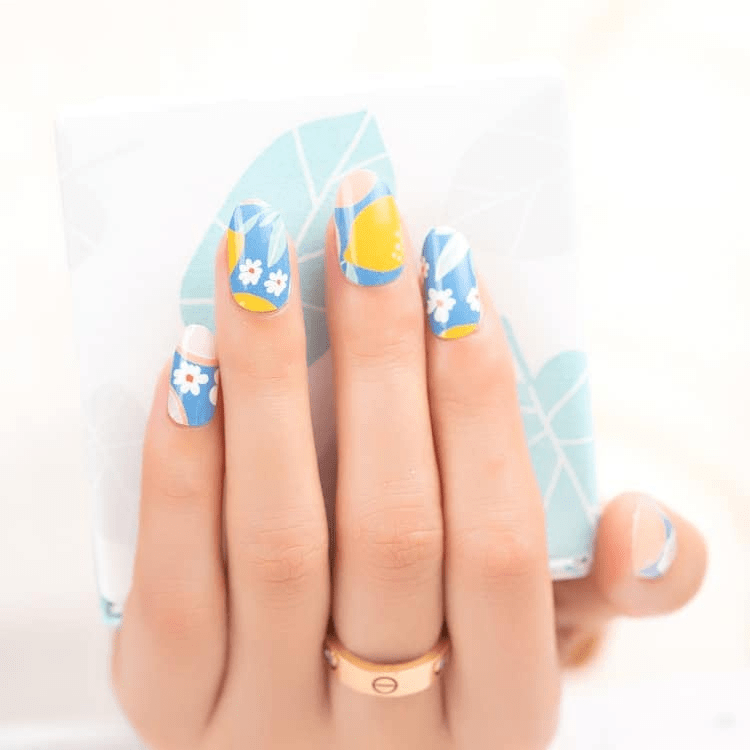 Blue nail wraps with fruit cocktail pattern featuring oranges and white flowers on hand