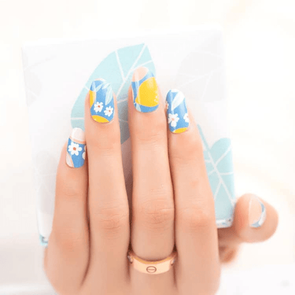 Blue nail wraps with fruit cocktail pattern featuring oranges and white flowers on hand