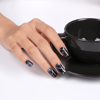 Hand wearing black and blue electric lightning nail wraps holding black coffee cup