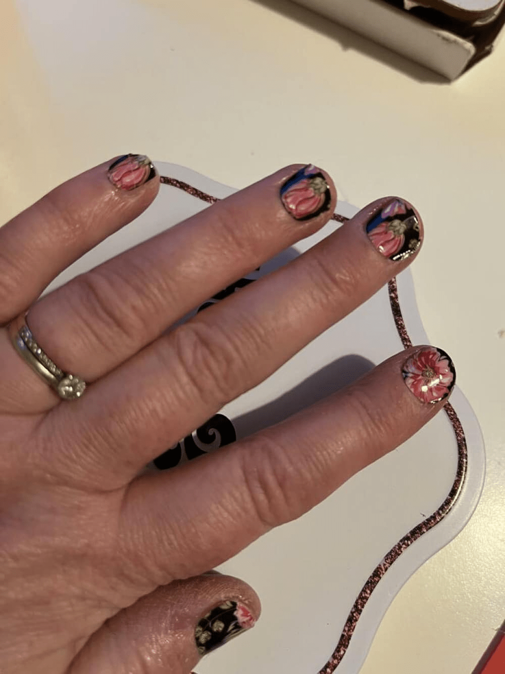 Hand displaying dark floral nail wraps with pink hibiscus flowers on black background