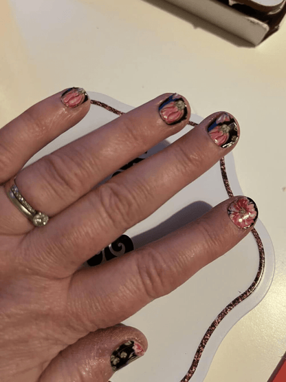 Hand displaying dark floral nail wraps with pink hibiscus flowers on black background