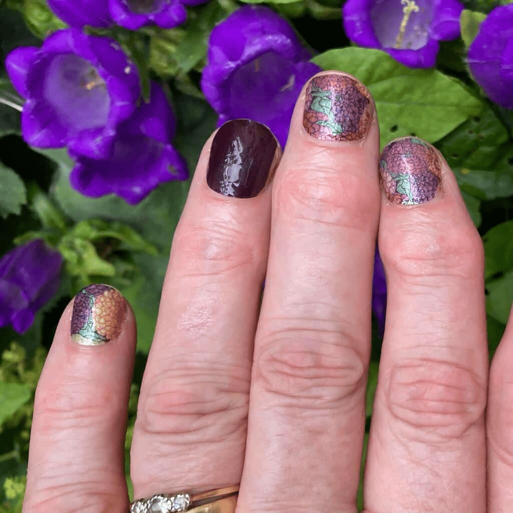 Hand with floral geranium nail wraps against purple flowers showing botanical manicure design