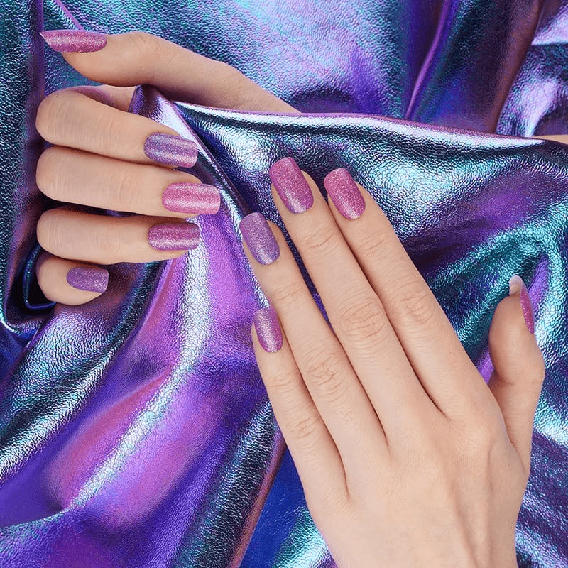 Hands wearing purple holographic glitter nail wraps against iridescent chrome fabric background