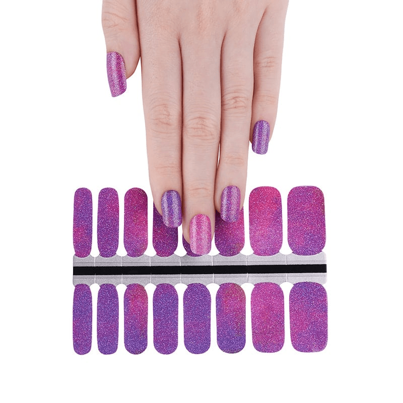 Hand with purple glitter nail wraps and full sheet of cosmic galaxy manicure wraps