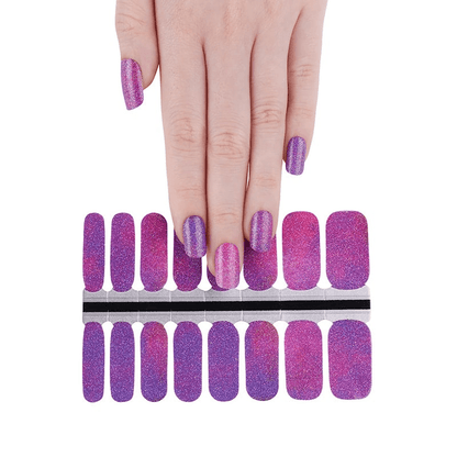 Hand with purple glitter nail wraps and full sheet of cosmic galaxy manicure wraps