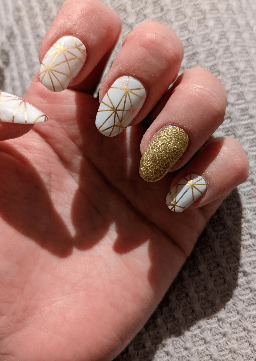 Hand wearing white and gold geometric nail wraps with glitter accent manicure