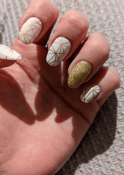 Hand wearing white and gold geometric nail wraps with glitter accent manicure