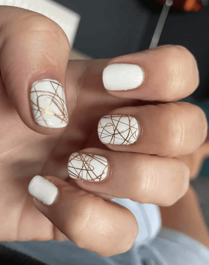 White and gold geometric nail wraps on hand showing elegant metallic line patterns