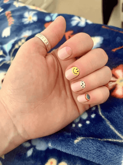 Hand wearing retro nail wraps with yellow smiley face and black white patterns